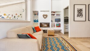 Una sala de estar con un sofá color beige, almohadas coloridas, un tapete estampado, un adorno con forma de corazón y un televisor.
