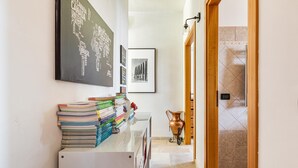 Un pasillo con una pizarra que muestra nombres de países, una fotografía enmarcada en la pared y una pila de libros sobre un mueble blanco.