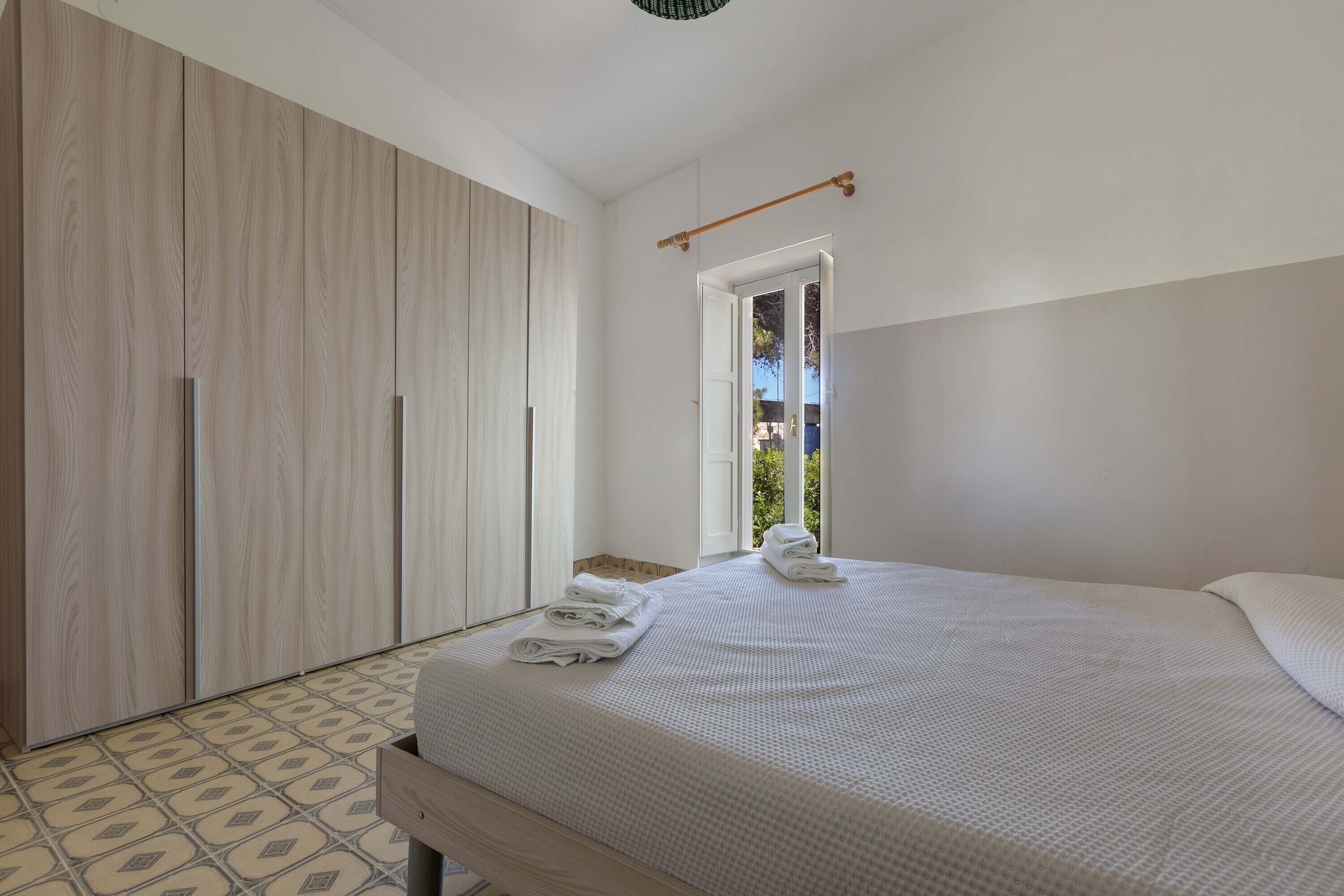 A bedroom with a bed, a wardrobe, and a window with a view of greenery.