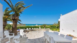 An outdoor patio with white wicker furniture, a stone floor, and a view of the sea. - 2374 Villa Costa Merlata by Perle di Puglia (Ostuni)