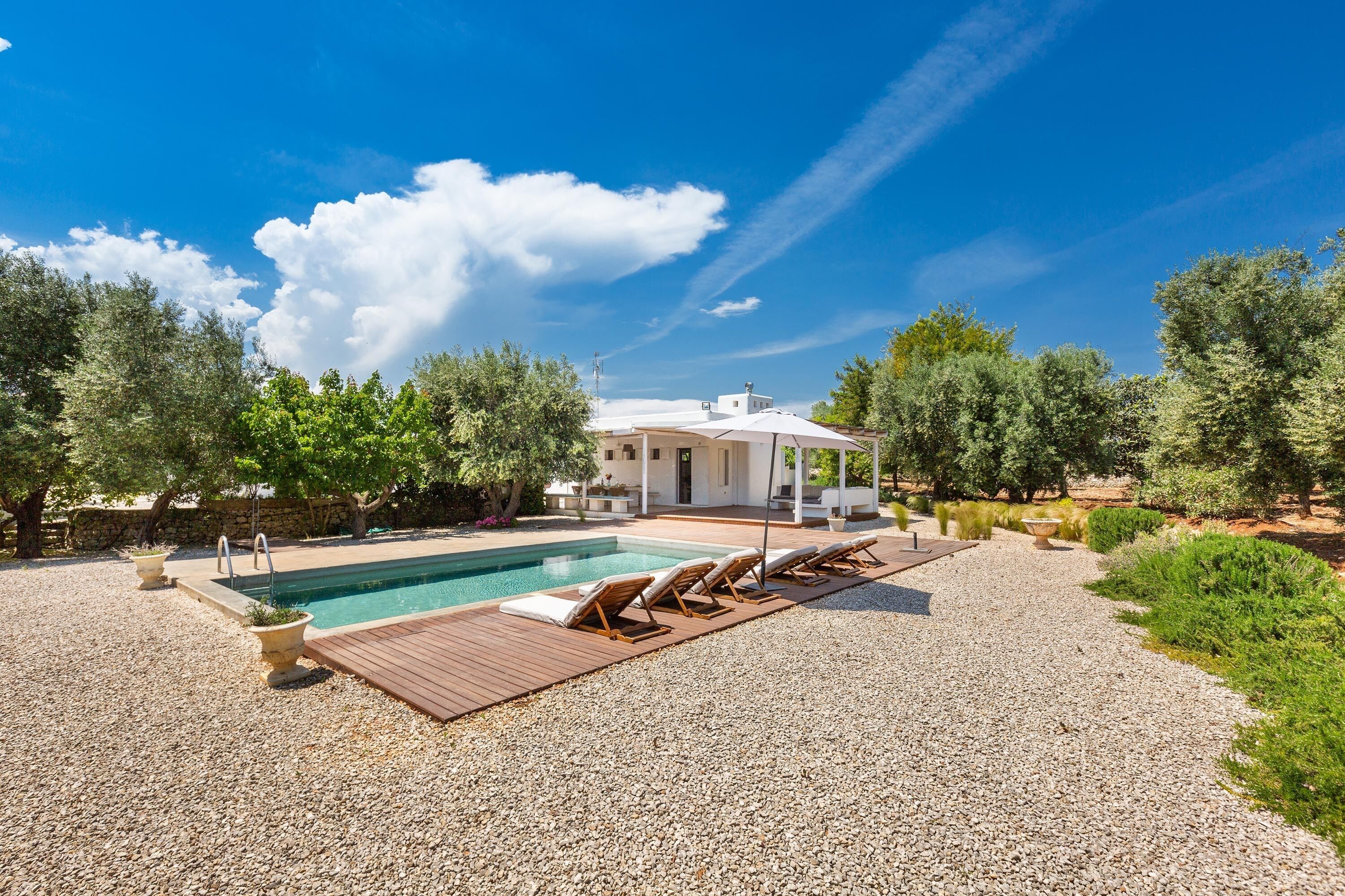 A pool area with a wooden deck, lounge chairs, and a stone pathway.