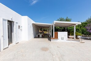 A modern white building with a covered patio area, a dining table, and a seating arrangement. - 2971 Villa Piti by Perle di Puglia (Carovigno)
