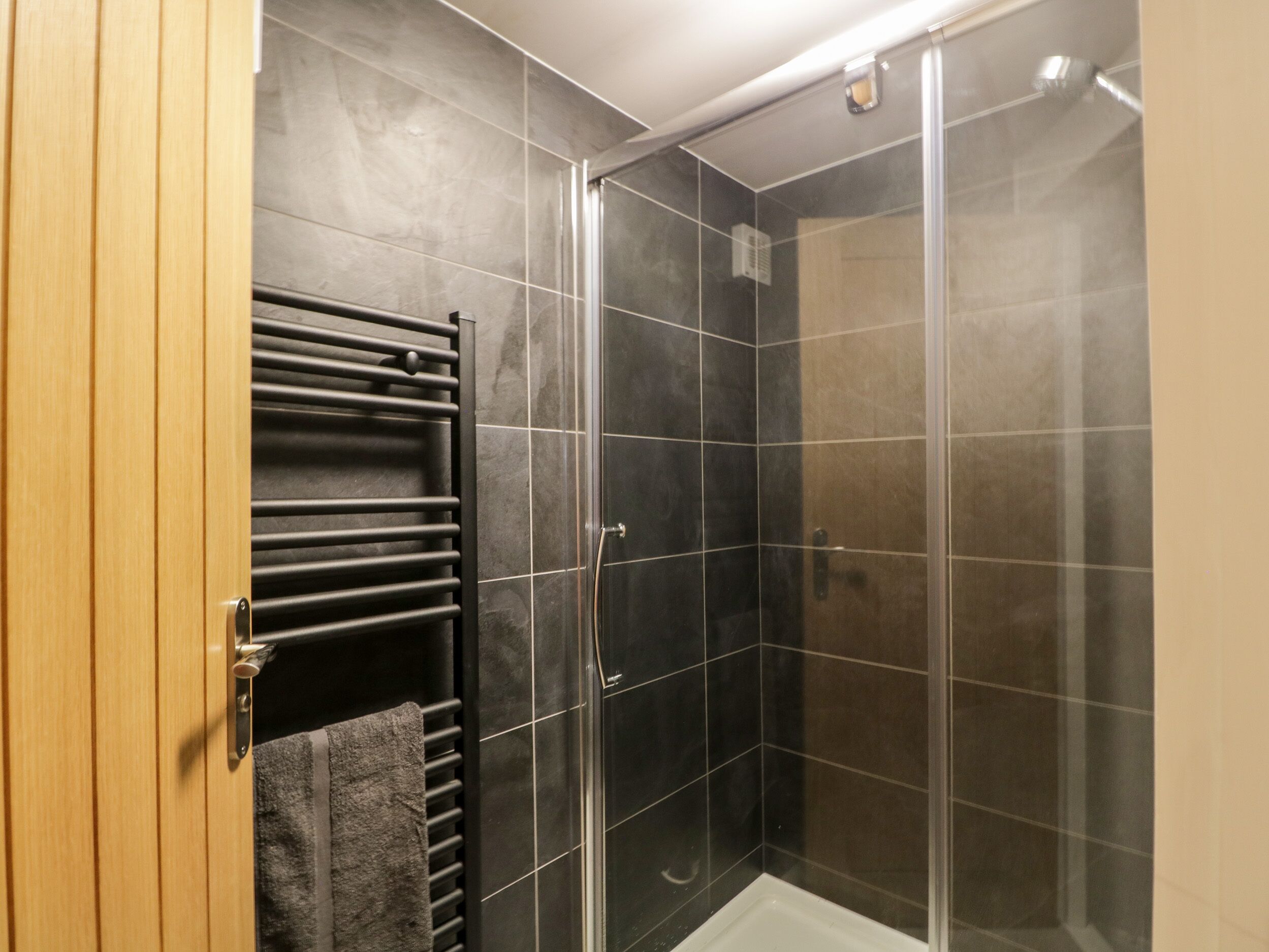 Een moderne badkamer met een douchecabine van glas, een handdoekhouder en een houten deur.