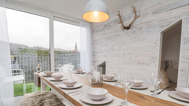 Ein moderner Essbereich mit einem langen Holztisch, der für eine Mahlzeit gedeckt ist, weißen Tellern und Weingläsern.