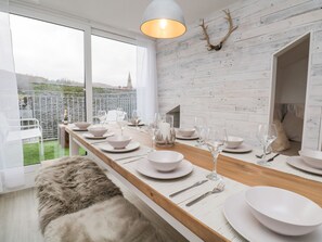 A modern dining area with a long wooden table set for a meal, white plates, and wine glasses. - Dixon Court (Ambleside)