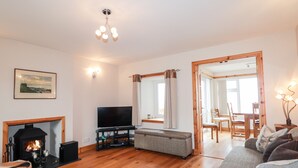 A living room with a fireplace, a television, a sofa, and a dining area with a table and chairs. - Learig (Buckie)