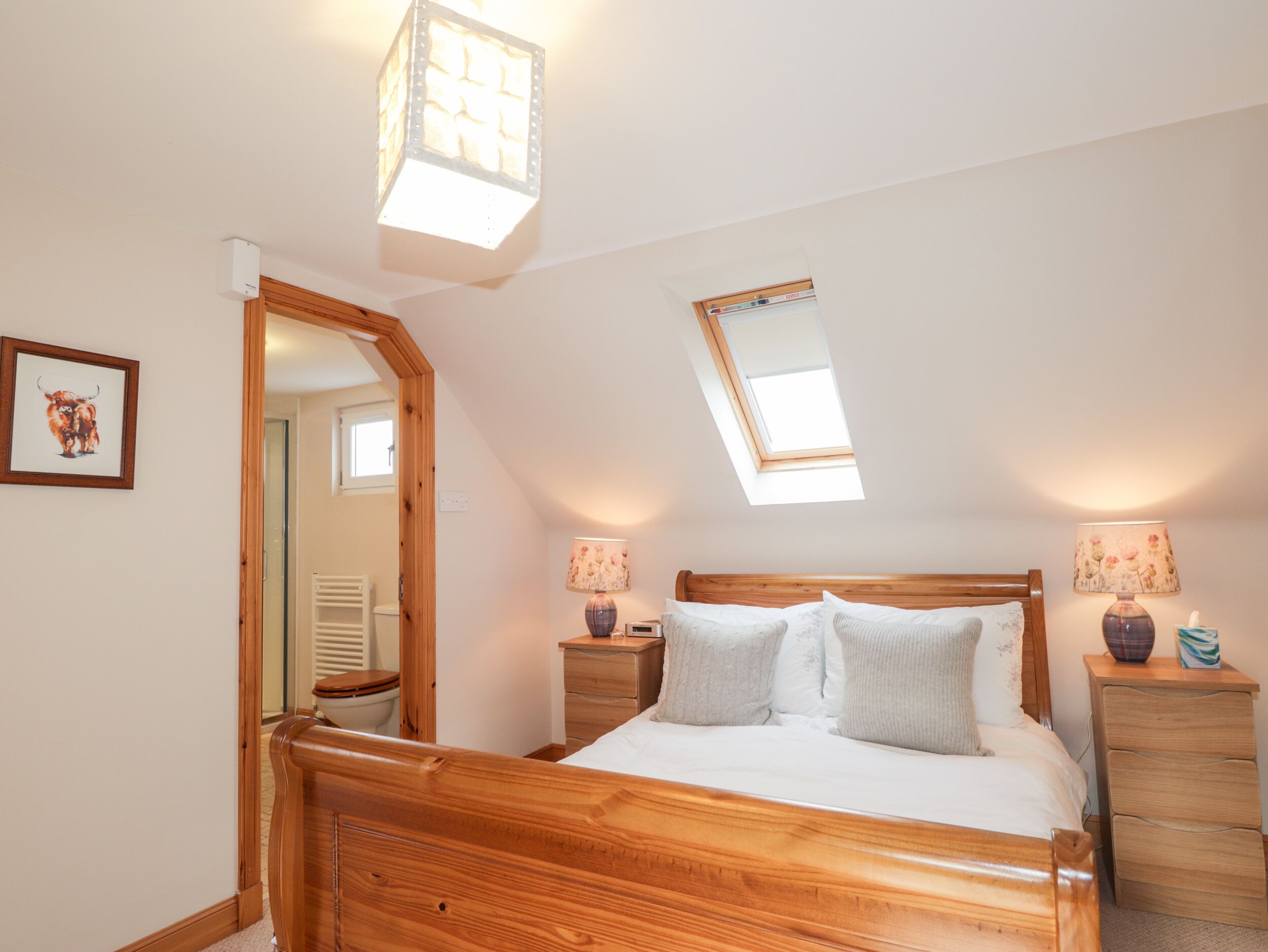 A bedroom with a wooden bed, a skylight, a bedside lamp, and a nightstand.