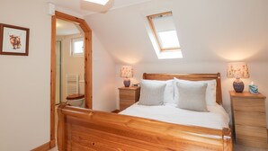 A bedroom with a wooden bed, a skylight, a bedside lamp, and a nightstand. - Learig (Buckie)
