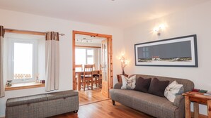 A living room with a sofa, a bench, a dining table with chairs, a chandelier, and a framed picture on the wall. - Learig (Buckie)