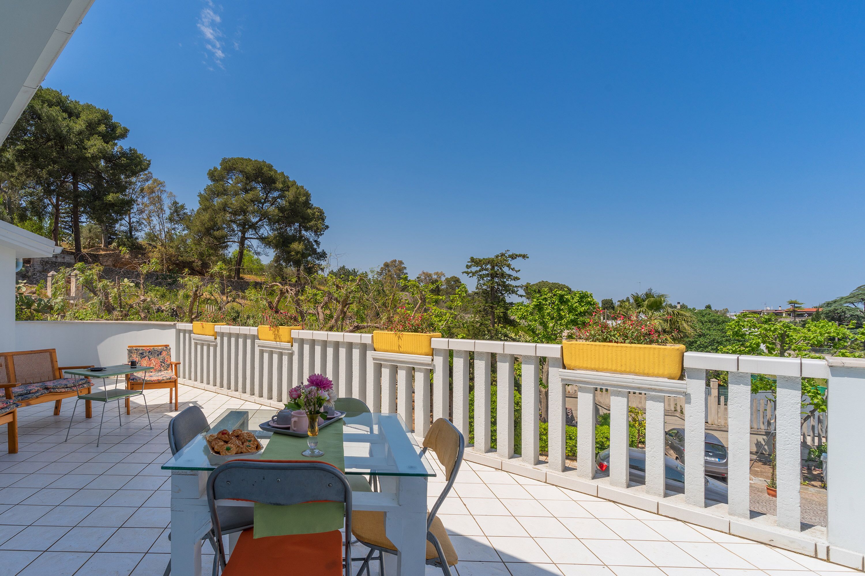Une terrasse avec une table et des chaises, une balustrade et une vue sur les arbres et les bâtiments.