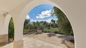 Un espacio al aire libre con un camino de piedra, arcos blancos y vistas a árboles y al cielo.