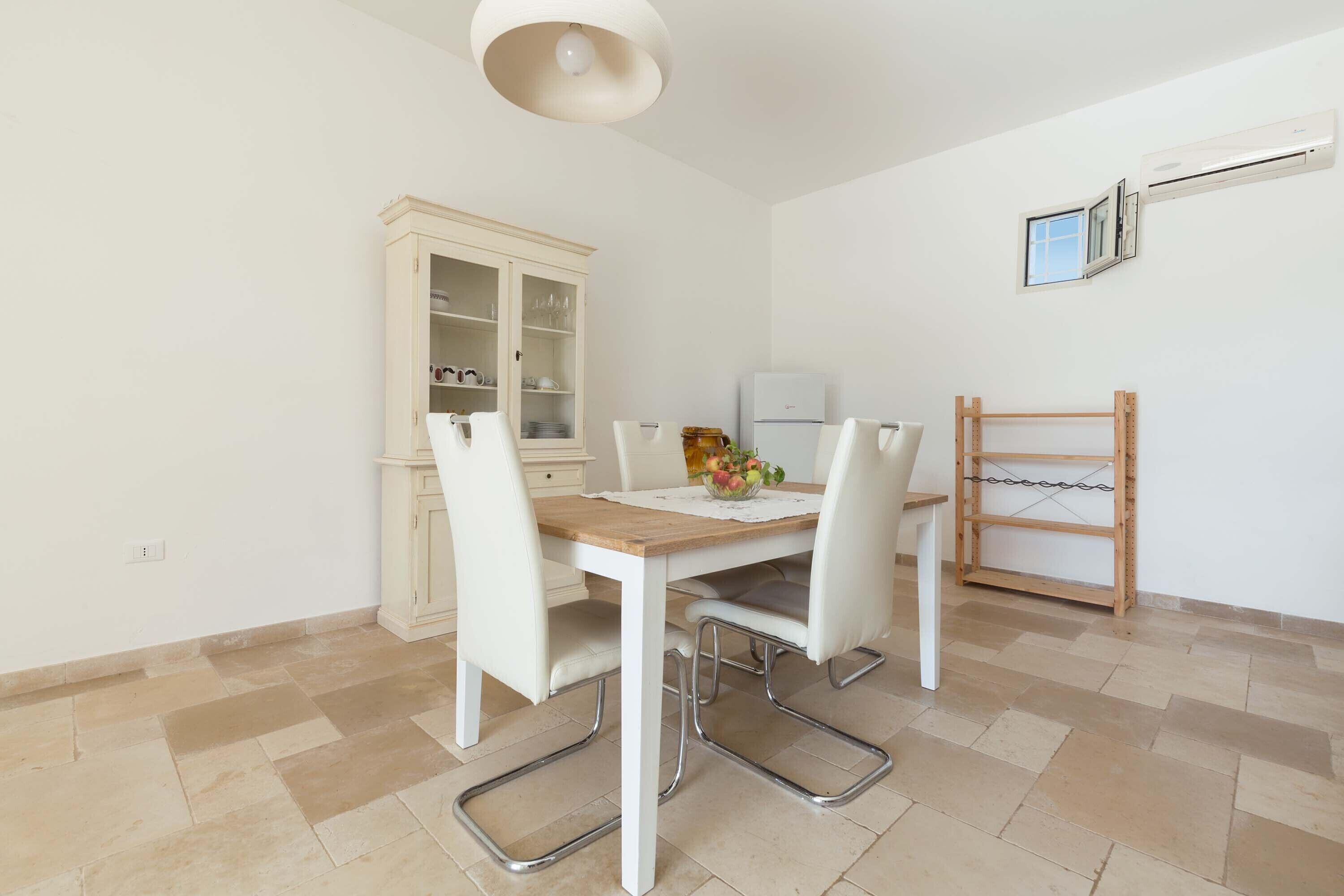 A dining area with a wooden table, white chairs, a cabinet, and a small refrigerator.