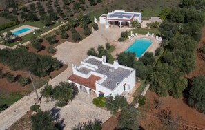 An aerial view of a property with two swimming pools, a covered patio, and a white building with a red roof.