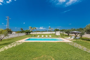 Piscina com espreguiçadeiras e um pérgola num quintal.