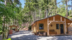 A wooden cabin with a gravel driveway, surrounded by tall trees. - Lady Bagots Cabin (Ruthin)