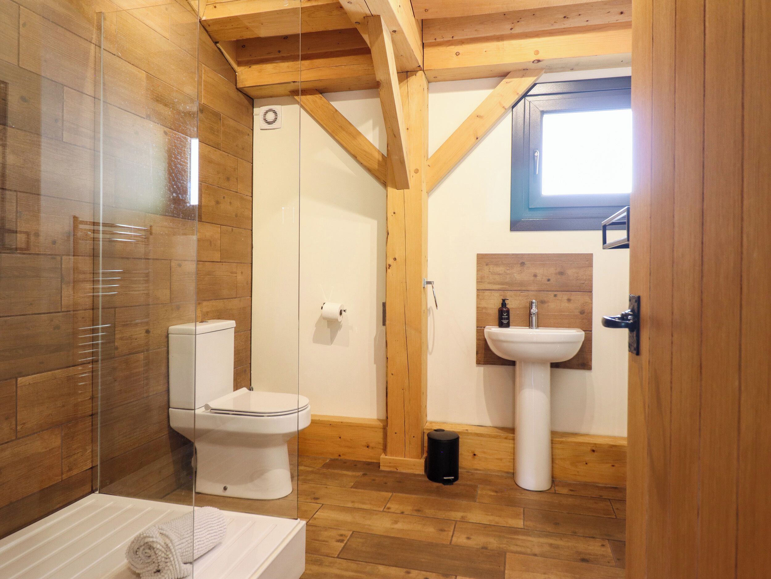 Un baño con cabina de ducha de vidrio, inodoro, lavabo y vigas de madera.