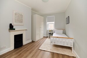A bedroom with a white bed, a fireplace, a wardrobe, and a framed artwork on the wall. - The Fulham Escape - Alluring 5BDR Flat (London)