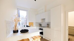 A modern kitchen with white cabinets, a central island with stools, and a window providing natural light. - The Fulham Escape - Alluring 5BDR Flat (London)
