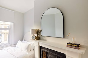 Une chambre à coucher avec un lit, une cheminée blanche, un grand miroir et une fenêtre.