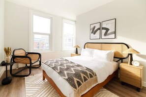 A bedroom with a bed, two chairs, a nightstand, a lamp, and two framed artworks on the wall. - The Fulham Escape - Alluring 5BDR Flat (London)
