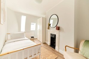 A bedroom with a bed, a chair, a fireplace, and a mirror on the wall. - The Fulham Escape - Alluring 5BDR Flat (London)