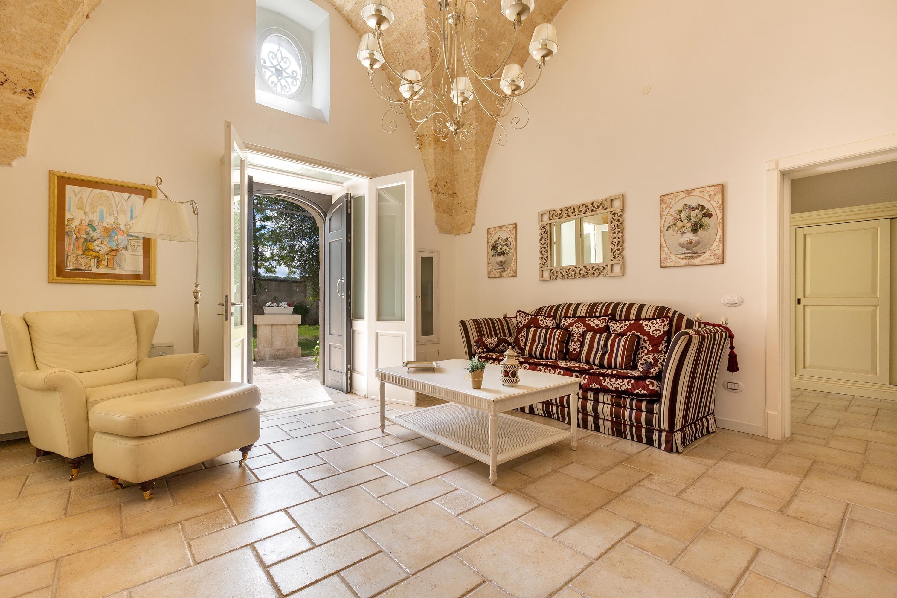 Un salon spacieux avec un fauteuil beige, un canapé à motifs, une table basse blanche et un lustre.