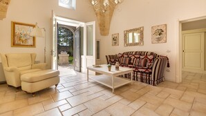 Un ampio soggiorno con una poltrona beige, un divano decorato, un tavolino da caffè bianco e un lampadario.
