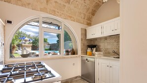 Cucina con piano cottura a gas, lavastoviglie, mobili bianchi e un'ampia finestra ad arco che si affaccia su un giardino.