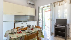 A compact kitchen with a dining area, a TV on a stand, and a sliding glass door leading to an outdoor area. - 2919 Il Bacio del Sole - Bilocale Concetta by Barbarhouse (Vieste)