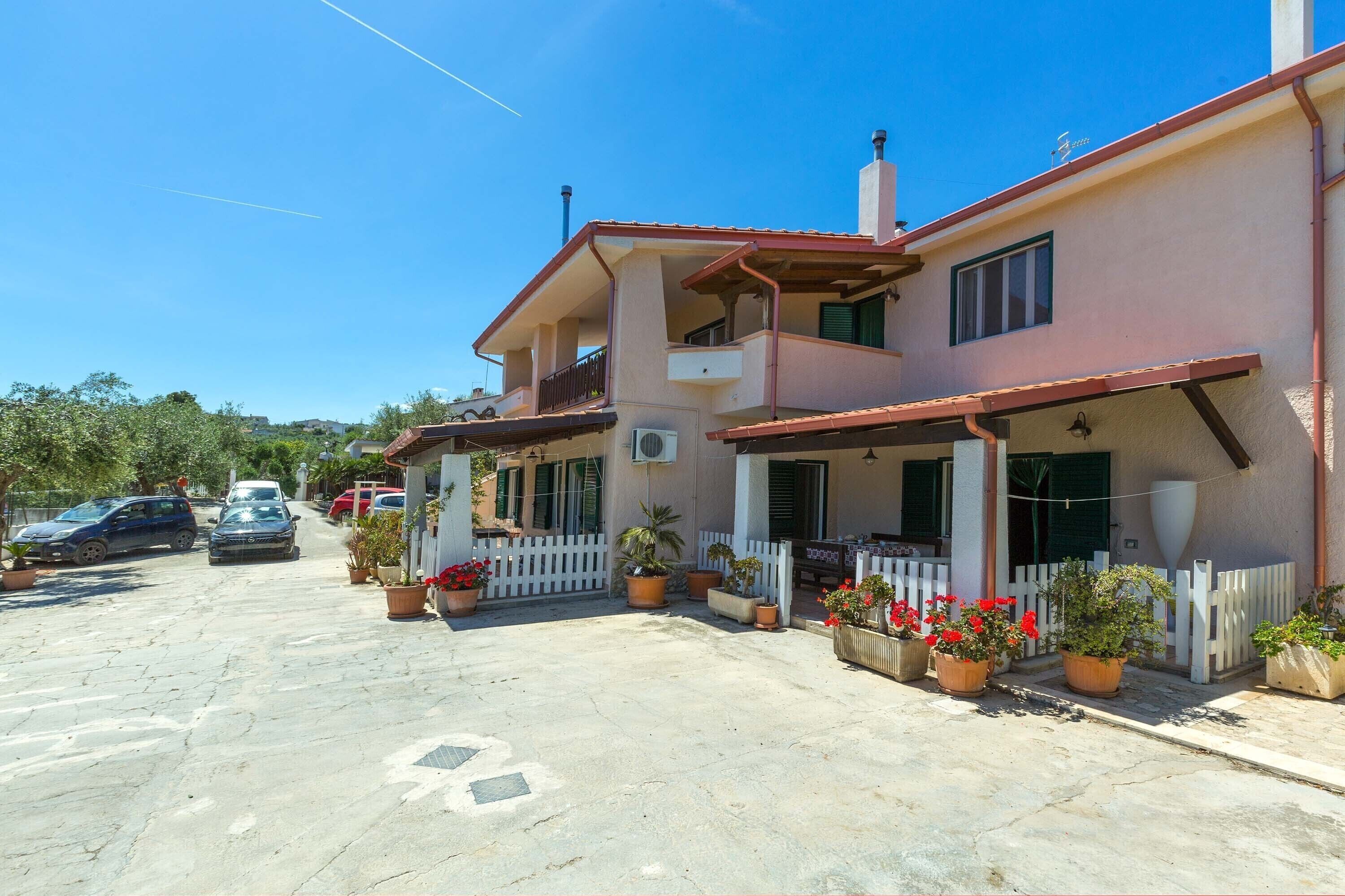 A two-story building with a balcony, a white picket fence, and potted plants.