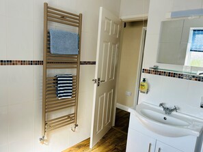 A bathroom with a wooden towel rack, a white sink with a mirror, and a tiled floor.