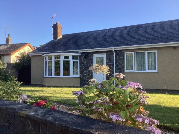 A single-story house with a stone facade, a bay window, and a small garden with flowers.