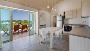 Een moderne keuken met een groot eiland, een zithoek met tafel en stoelen, en uitzicht door de glazen deuren.