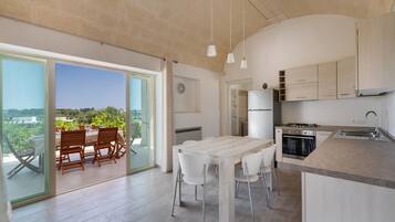 Cozinha moderna com uma ilha grande, área de jantar com mesa e cadeiras, e vista através das portas de vidro.