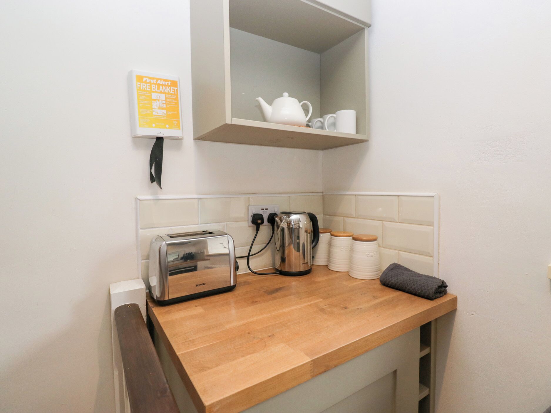 Une petite cuisine équipée d’un grille-pain, d’une bouilloire et de tasses à thé, le tout posé sur le plan de travail.