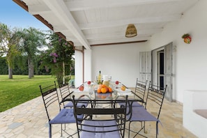 Een terras met een glazen tafel, metalen stoelen en een stenen vloer.