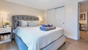 Ein Schlafzimmer mit einem gebügelten, gestreiften Bett, einer Nachttischlampe, einem Zimmerpflänzchen und Nachttisch.