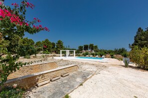 A pool area with a white gazebo, stone steps, and surrounding greenery.