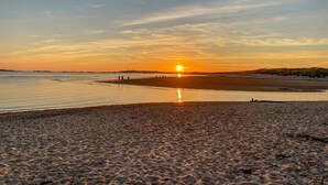 Une plage où le soleil se couche à l’horizon, avec une eau calme et des gens qui se promènent le long du rivage.