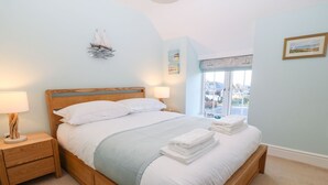 Un lit bien fait, avec du linge de lit blanc et un plaid bleu, des tables de chevet en bois avec des lampes, une décoration sur le thème de la voile et une fenêtre donnant sur l’extérieur.