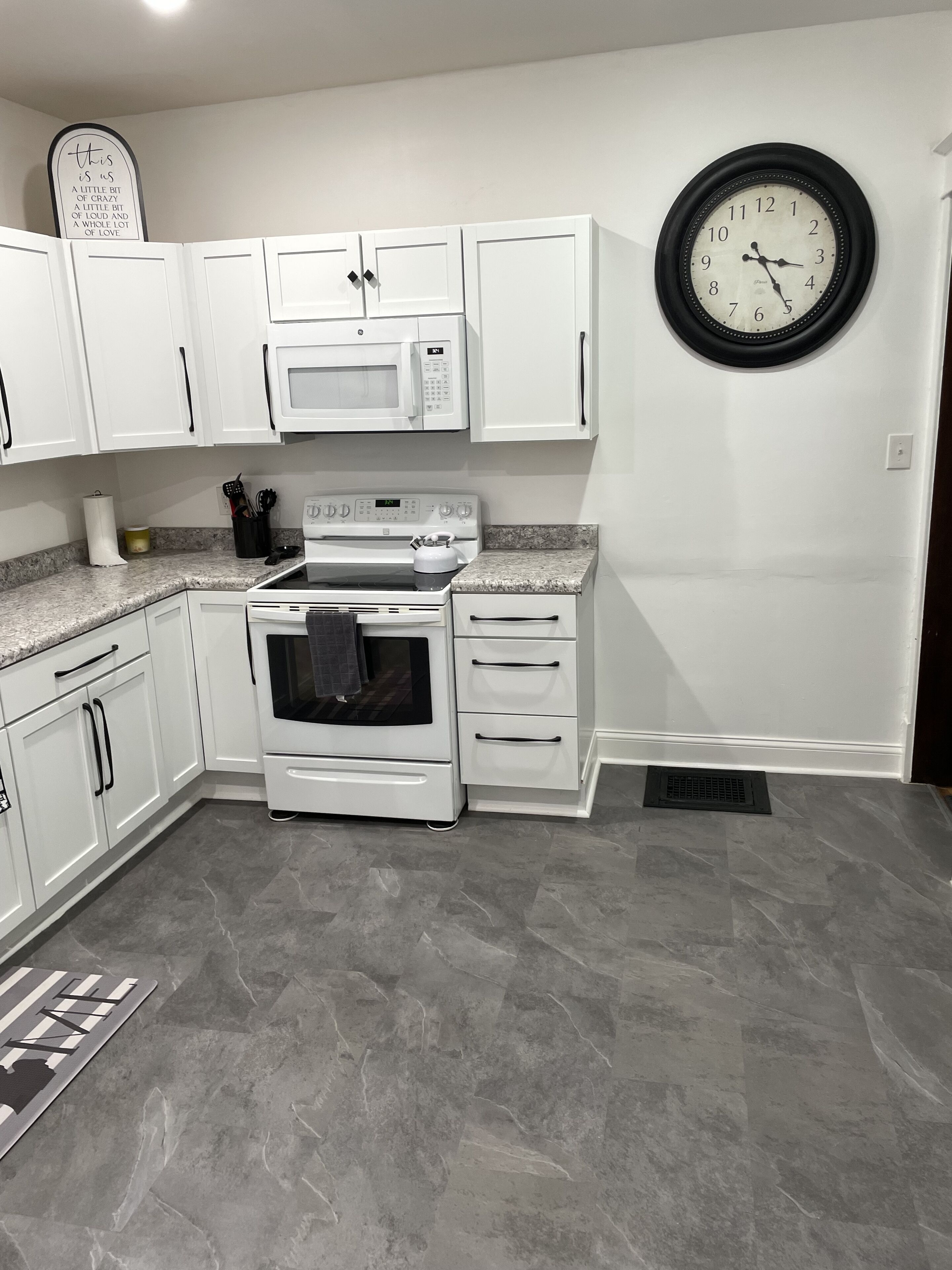 A kitchen with white cabinets, a microwave, stove, and a clock on the wall.