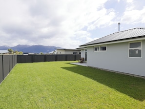 A residential backyard with a fenced area, a lawn, and a house with a metal roof.