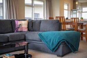 A modern living room with a grey sectional sofa, a teal throw blanket, and a coffee table with books.