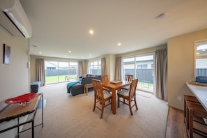 A spacious living area with a dining table, chairs, a sofa, and a red chair. - Fiordland Getaway - Te Anau Holiday Home (Te Anau)
