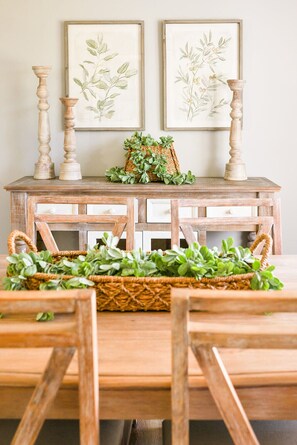 Una mesa de madera rústica con dos láminas enmarcadas de motivos botánicos, una cesta tejida con follaje y dos candelabros.