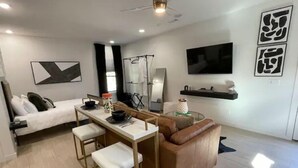 Ein modernes Wohnzimmer mit Essbereich, einer Couch, einem Couchtisch und einem an der Wand befestigten Fernseher.