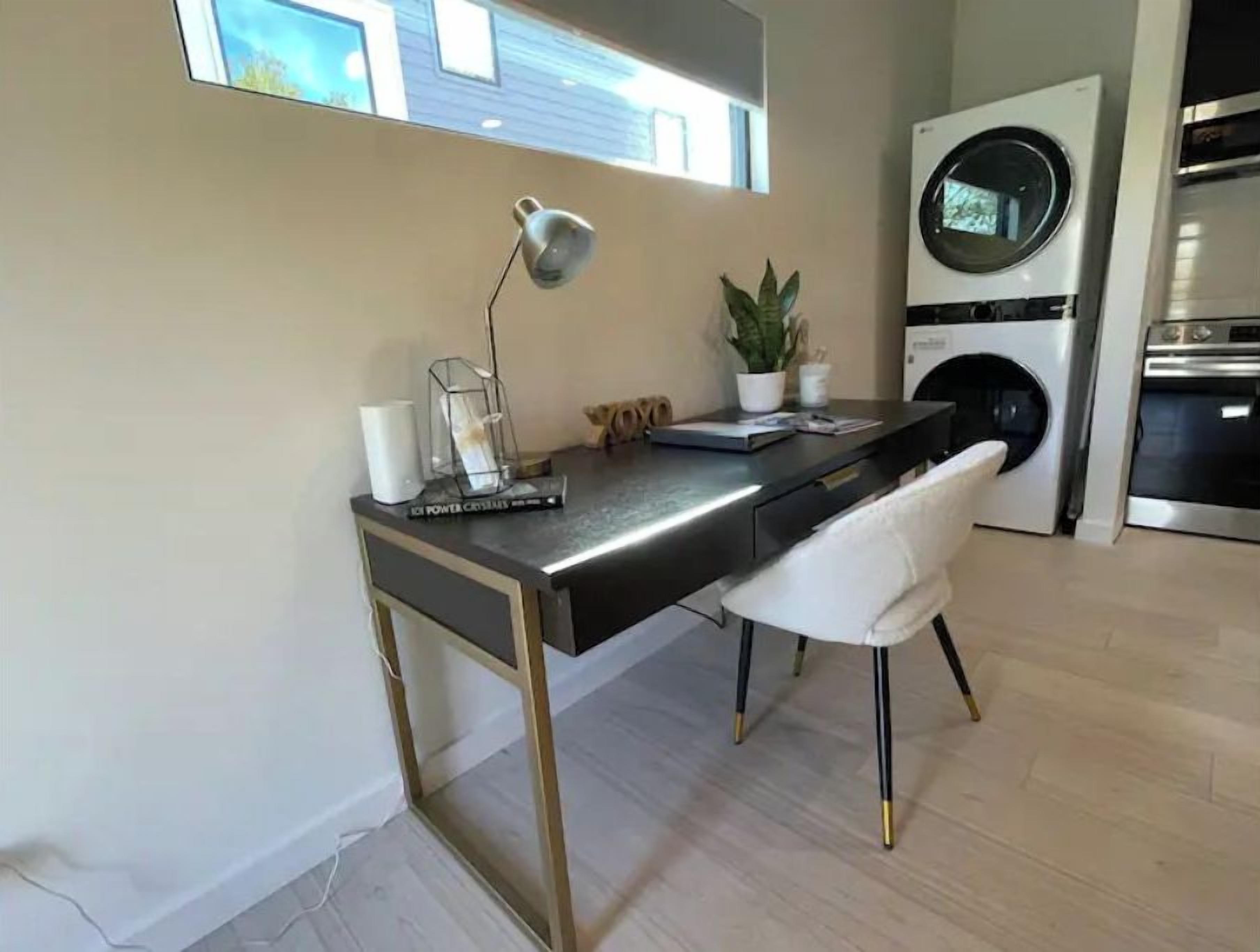 A modern kitchen with a built-in washing machine, a desk with a lamp, and a potted plant.