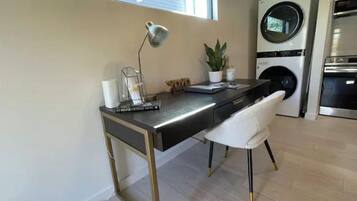 A modern kitchen with a built-in washing machine, a desk with a lamp, and a potted plant.