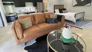 Ein modernes Wohnzimmer mit einem braunen Ledersofa, einem Glastisch und einem Bett mit weißer Bettwäsche.