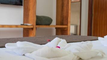 Una habitación de hotel con cama, estante de madera, perchero y un cuadro en la pared.